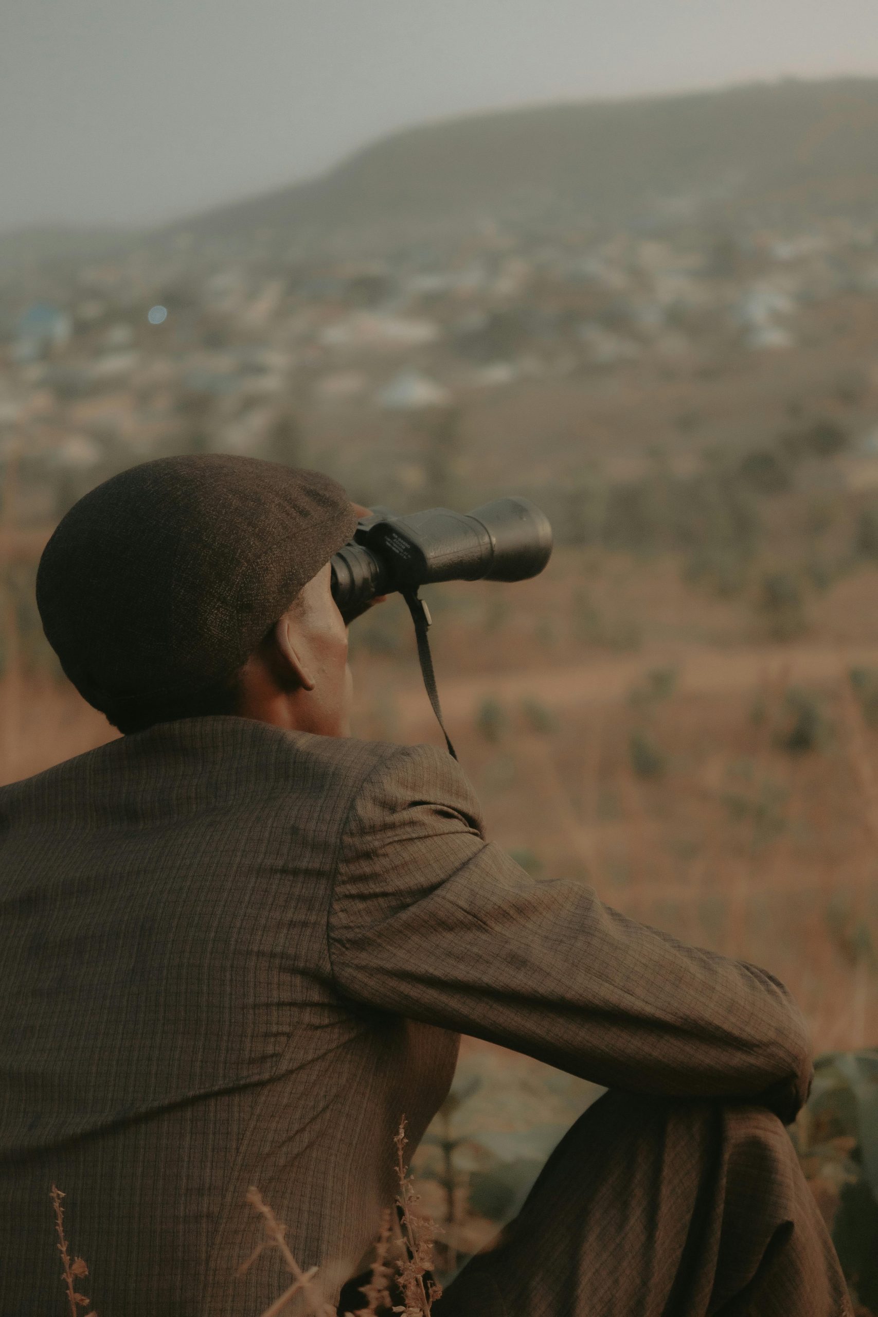 Un homme portant un chapeau observe au loin avec des jumelles en extérieur.
