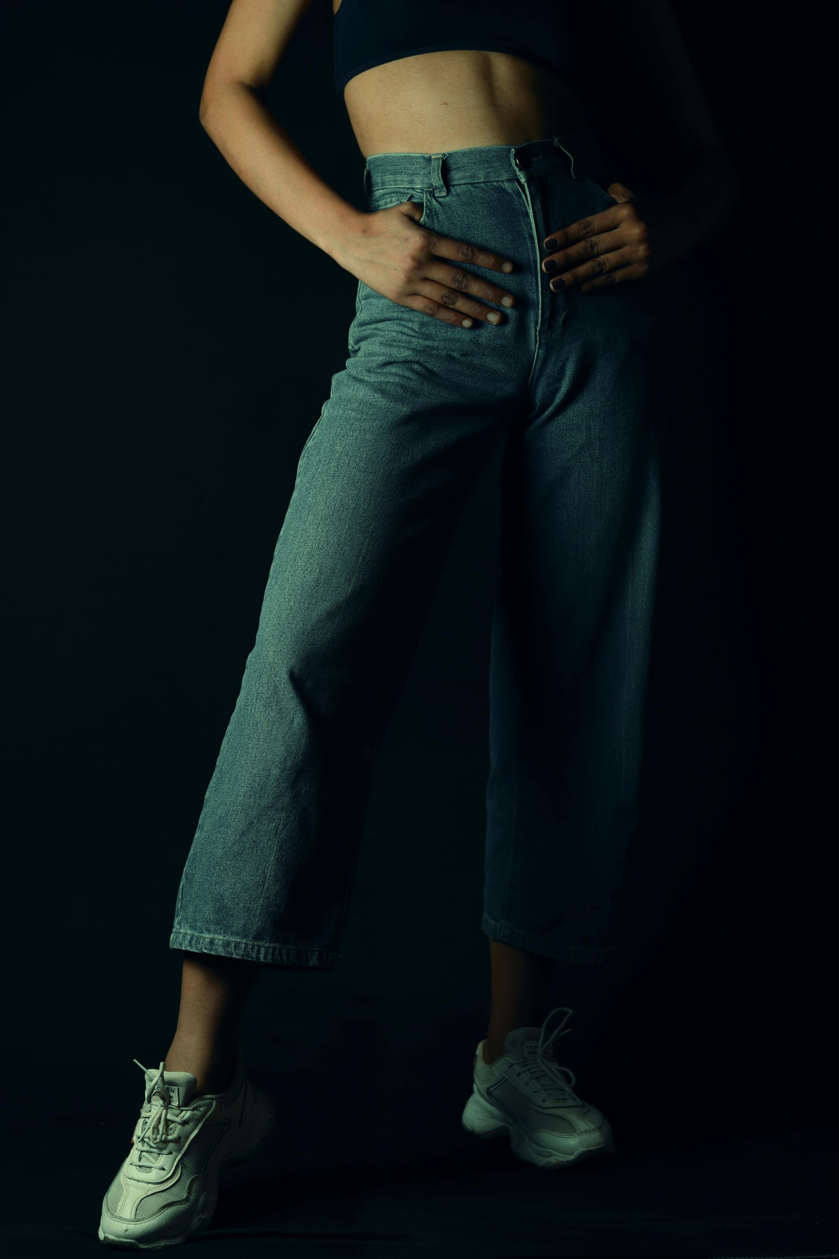 Stylish woman posant en jean et soutien-gorge de sport avec des baskets blanches sous un éclairage dramatique