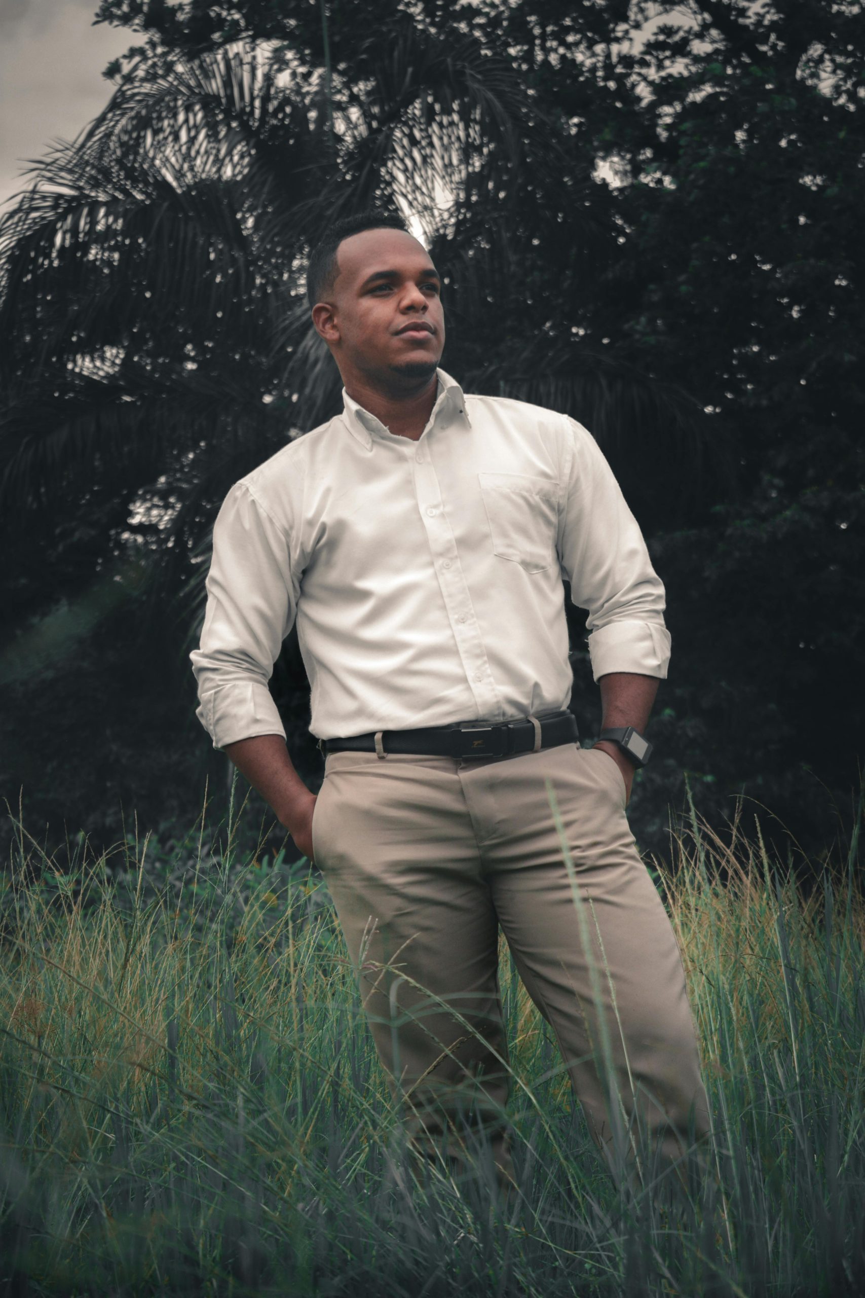 Un homme élégant en chemise blanche et pantalon kaki se tient avec assurance dans un champ.