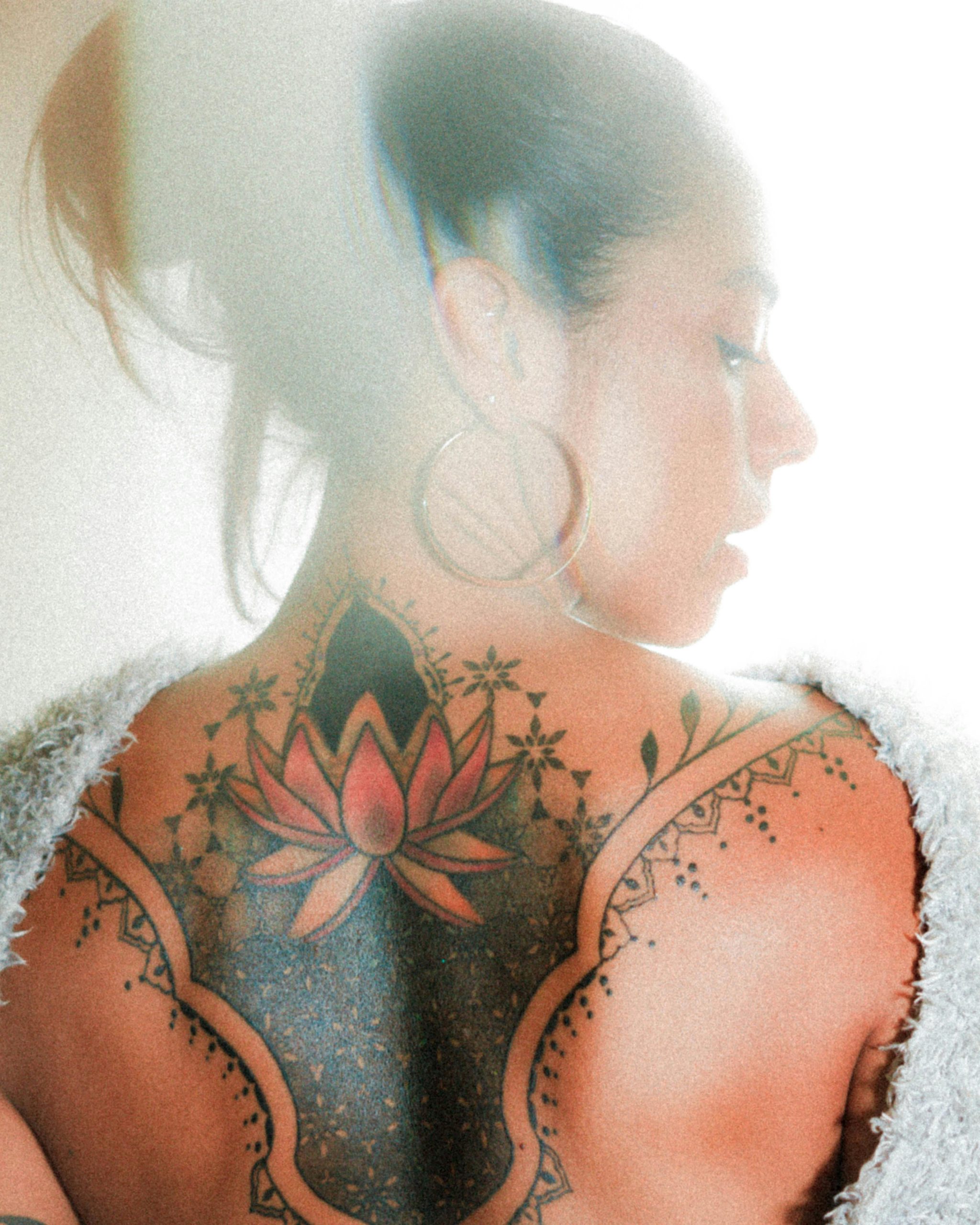 Un profil de femme montrant un tatouage coloré de lotus sur son dos.