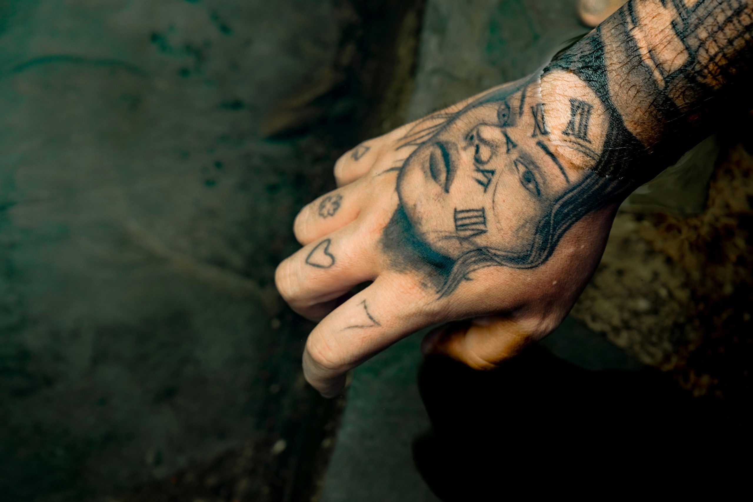 A detailed shot of a hand with expressive tattoos including Roman numerals and faces. Une photo détaillée d'une main avec des tatouages expressifs incluant des chiffres romains et des visages.