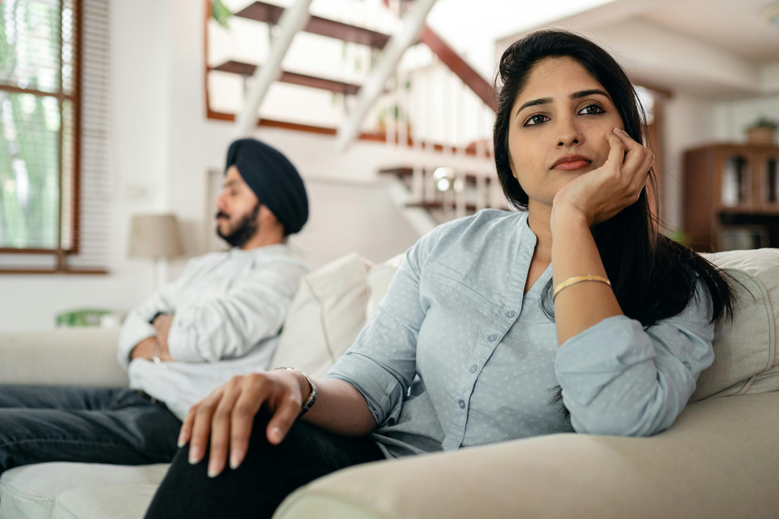 Young Indian couple sitting on different sides of couch and ignoring each other after arguing at home Jeune couple indien assis de part et d'autre du canapé et s'ignorant mutuellement après une dispute à la maison