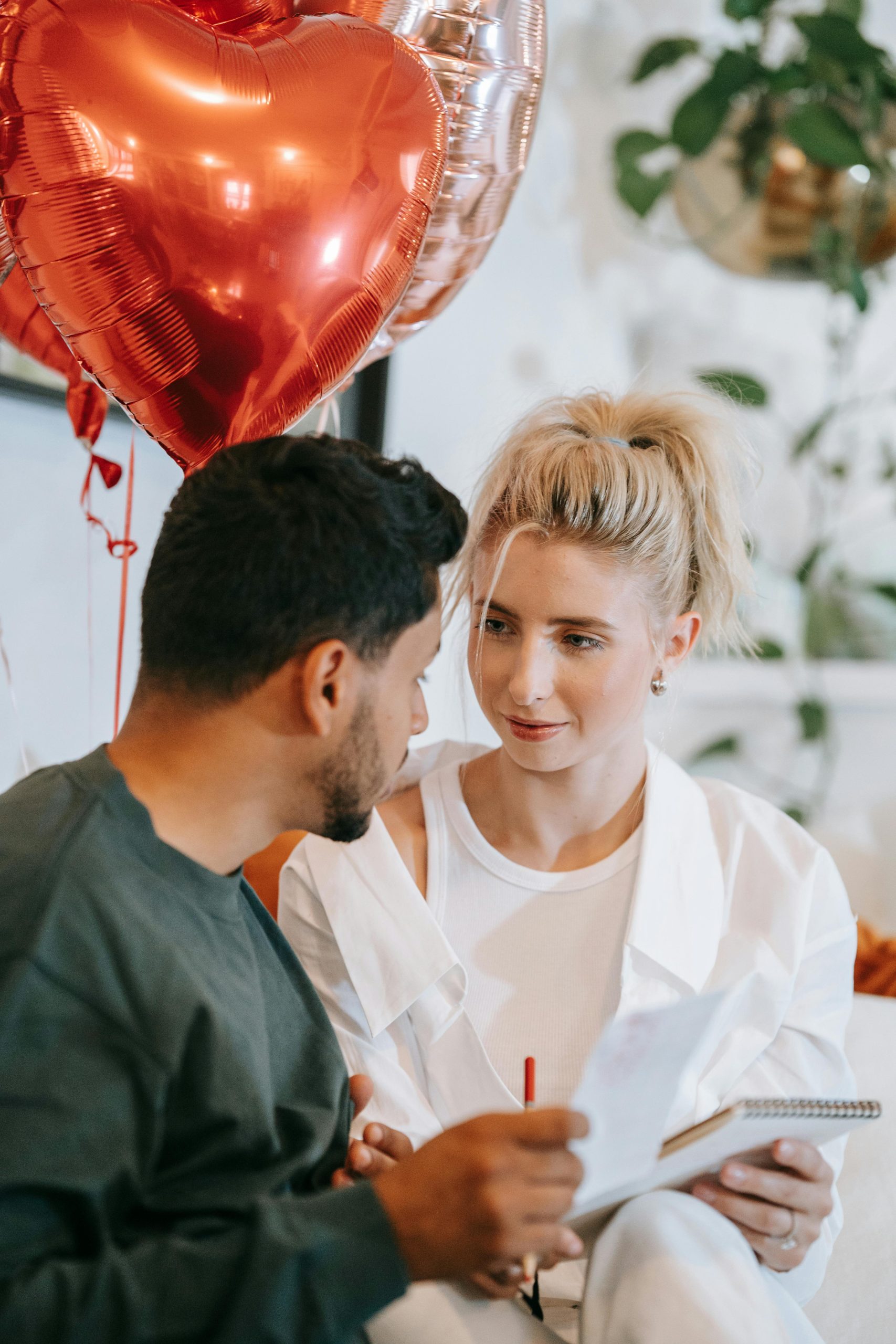 Couple assis avec des ballons en forme de cœur rouge à l'intérieur, partageant un moment romantique.