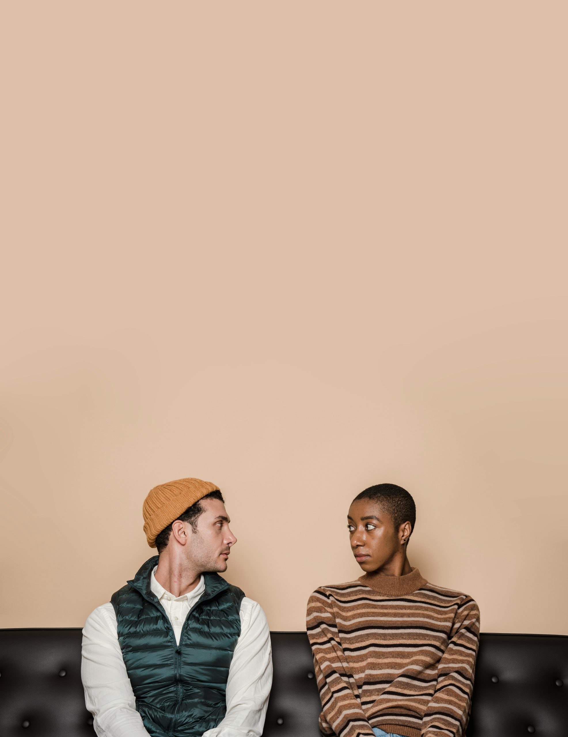 Misunderstanding multiethnic couple having problems in relationship sitting on leather couch and looking at each other against beige background Couple multiethnique en incompréhension ayant des problèmes relationnels assis sur un canapé en cuir et se regardant sur un fond beige