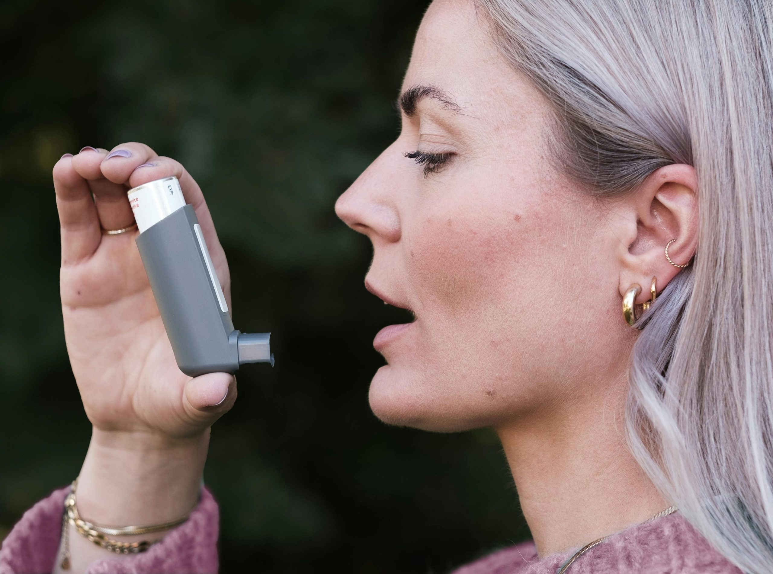 Close-up profile shot of a woman using an asthma inhaler outdoors, highlighting healthcare essentials. Gros plan de profil d'une femme utilisant un inhalateur d'asthme à l'extérieur, mettant en évidence les essentiels des soins de santé.