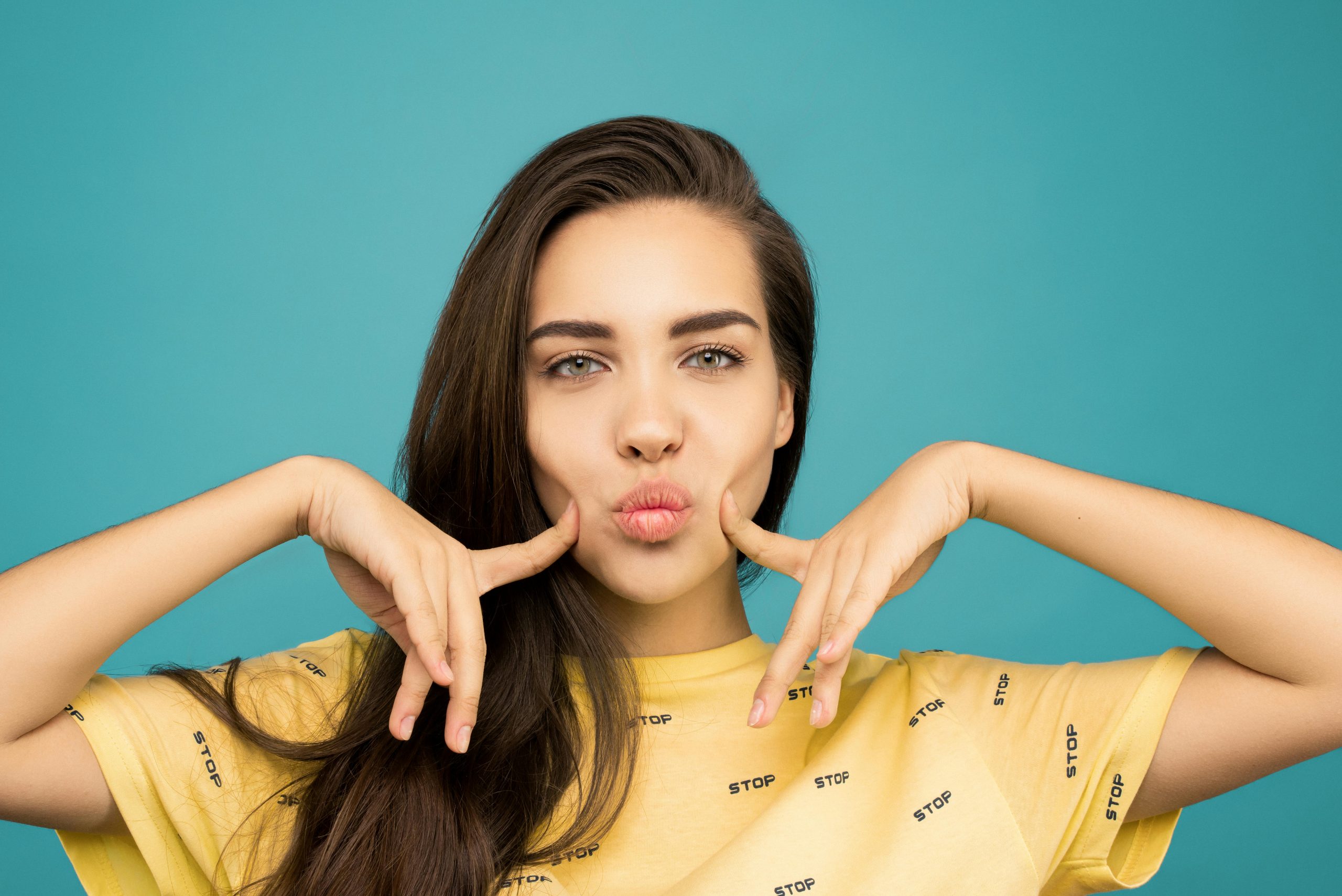 Vibrant portrait of a woman posing playfully against a blue background, wearing a yellow t-shirt. Portrait vibrant d'une femme posant de manière ludique sur fond bleu, portant un t-shirt jaune.