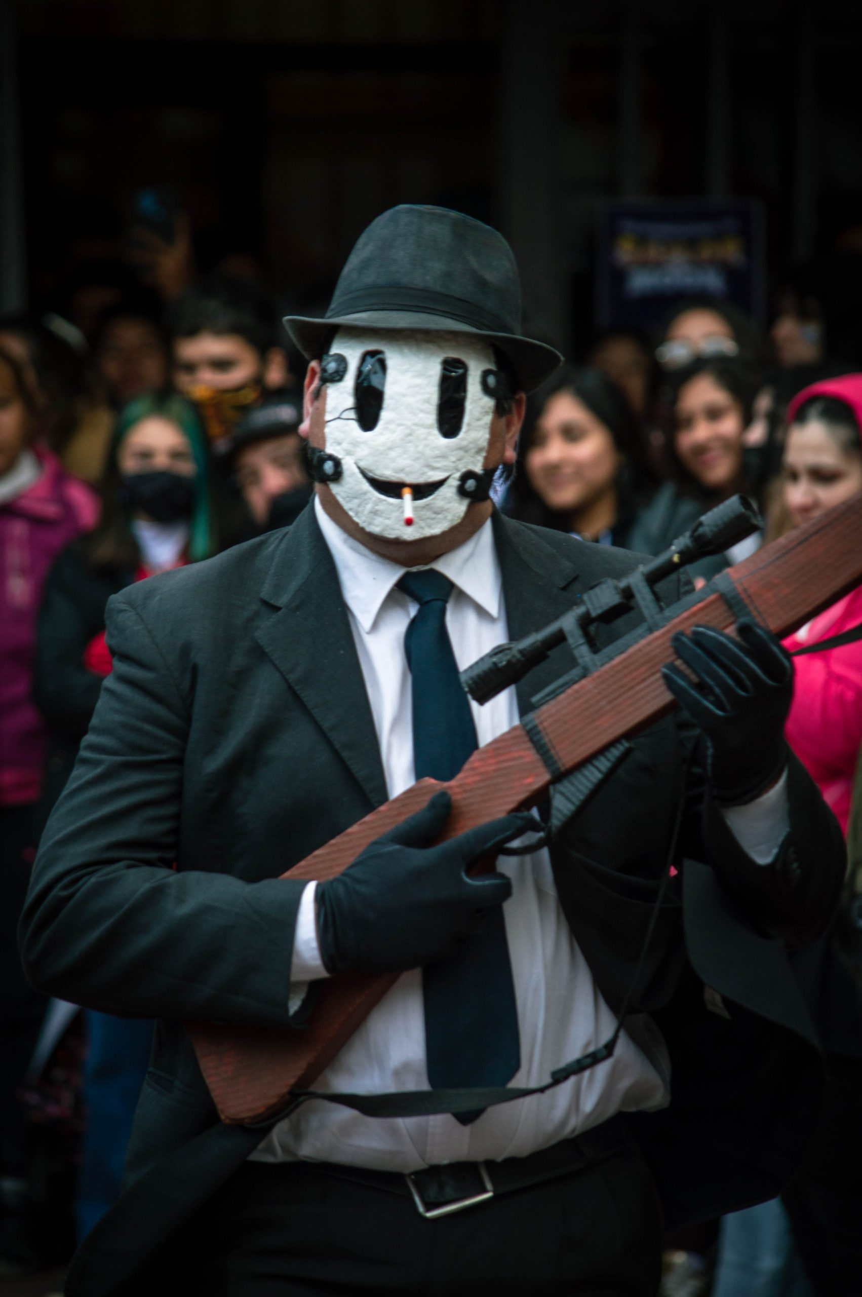 Man in a mask and suit holds a fake rifle during a cosplay event. Homme en masque et costume tenant un faux fusil lors d'un événement de cosplay.