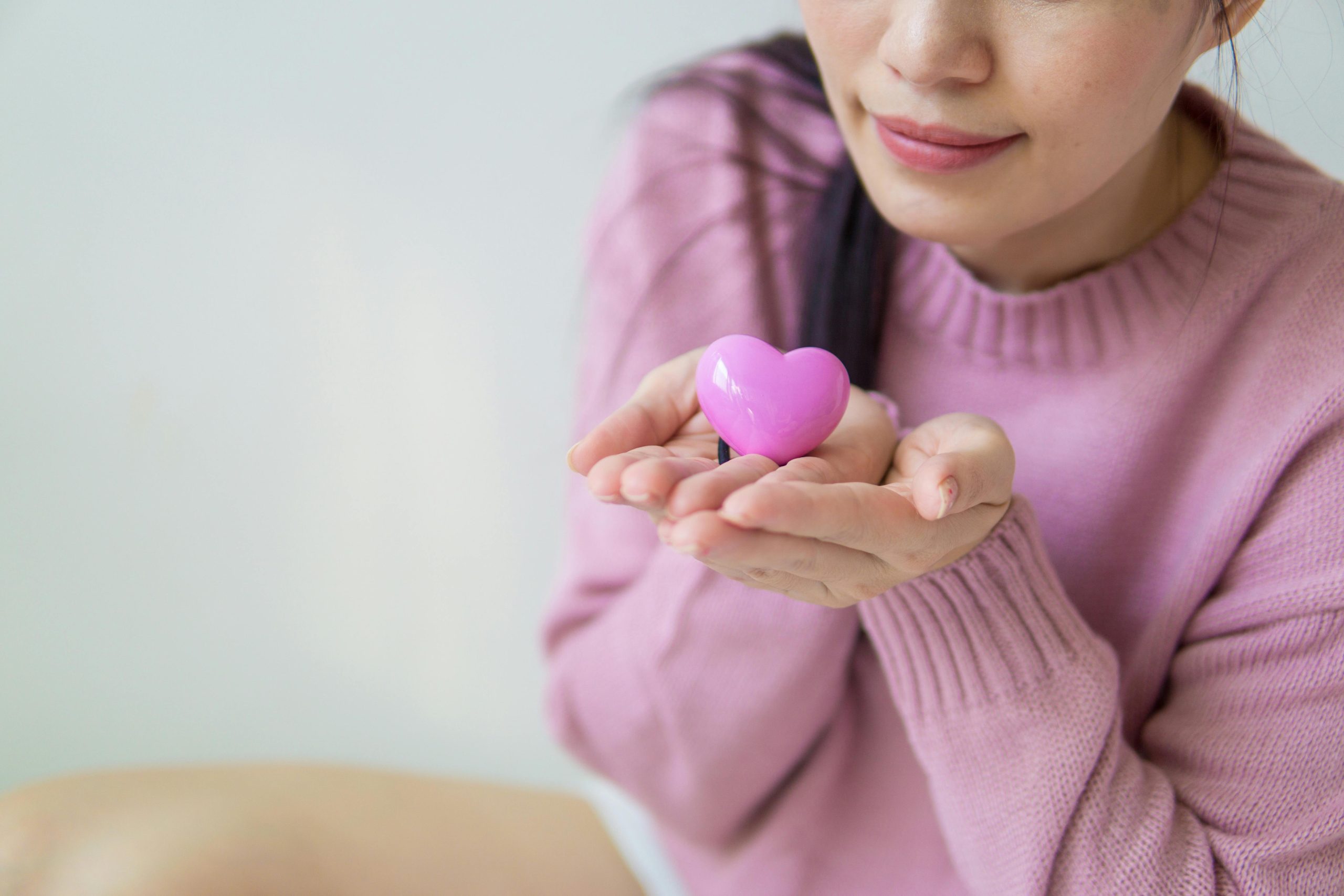 A woman in a pink sweater holding a pink heart-shaped toy, symbolizing love and kindness. Une femme dans un pull rose tenant un jouet en forme de cœur rose, symbolisant l'amour et la bienveillance.