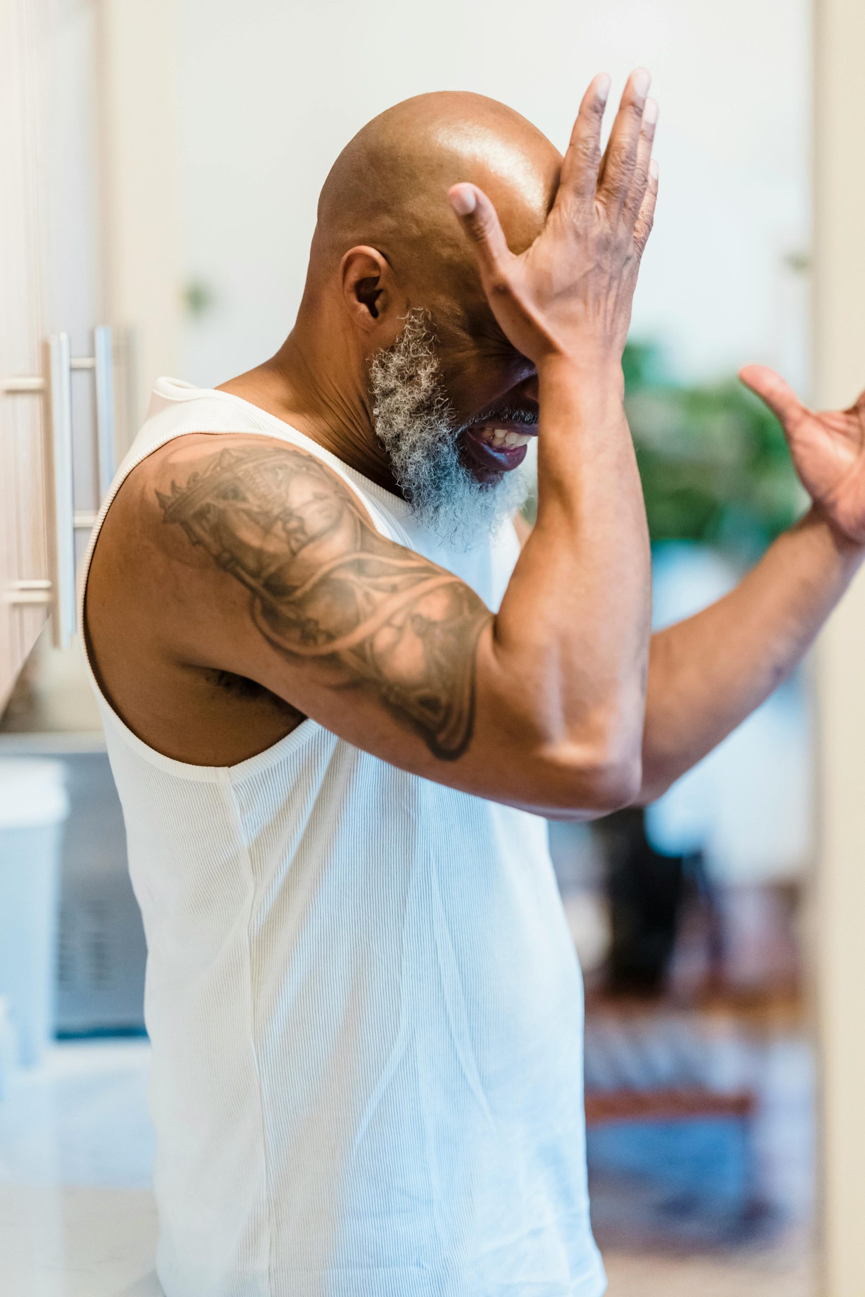 An adult man with a tattoo expresses stress and regret in an indoor setting. Un homme adulte avec un tatouage exprime le stress et les regrets dans un cadre intérieur.