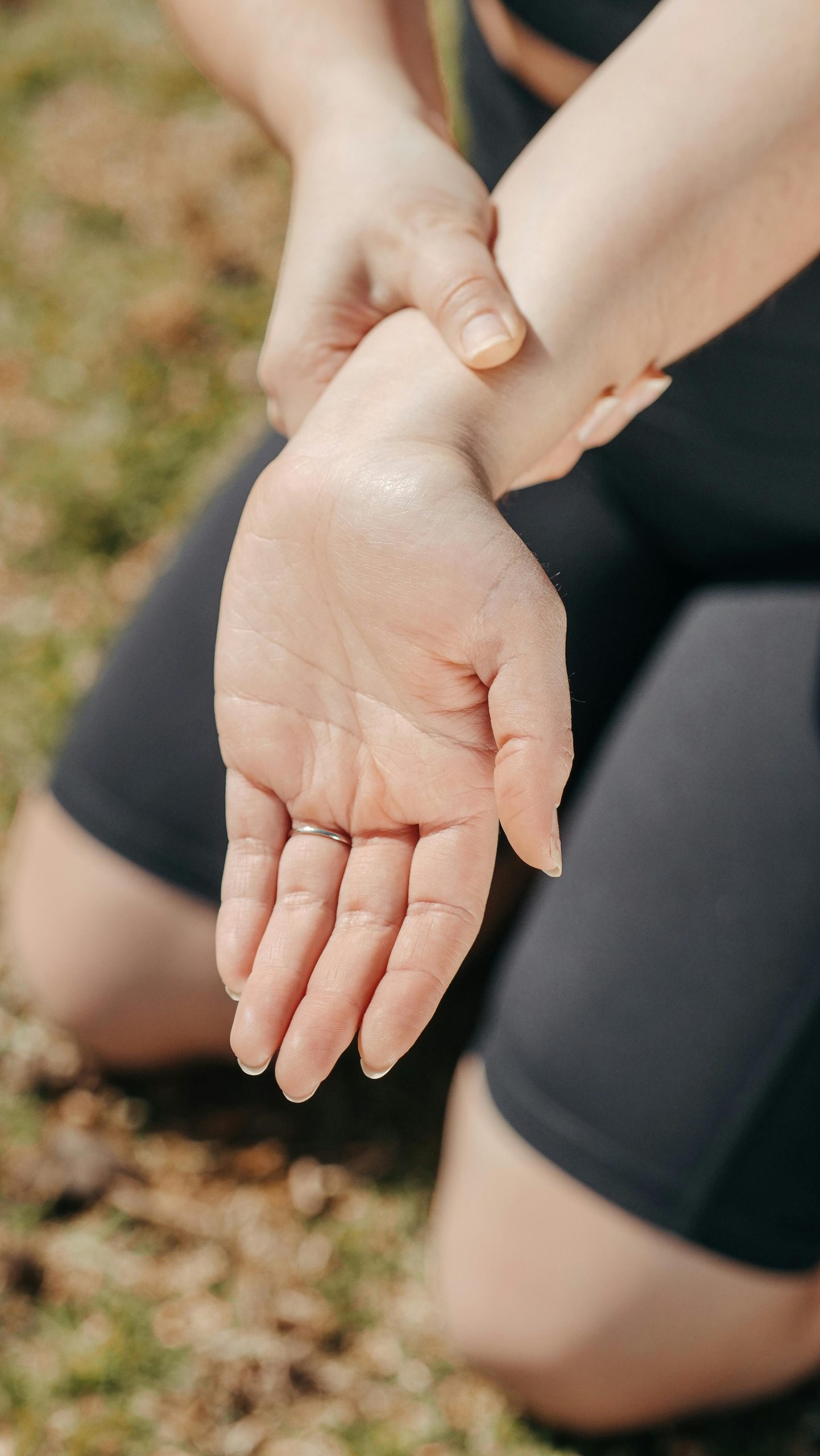 Close-up of a woman's hand holding her wrist outdoors, symbolizing injury or pain relief. Gros plan de la main d'une femme tenant son poignet à l'extérieur, symbolisant une blessure ou un soulagement de la douleur.