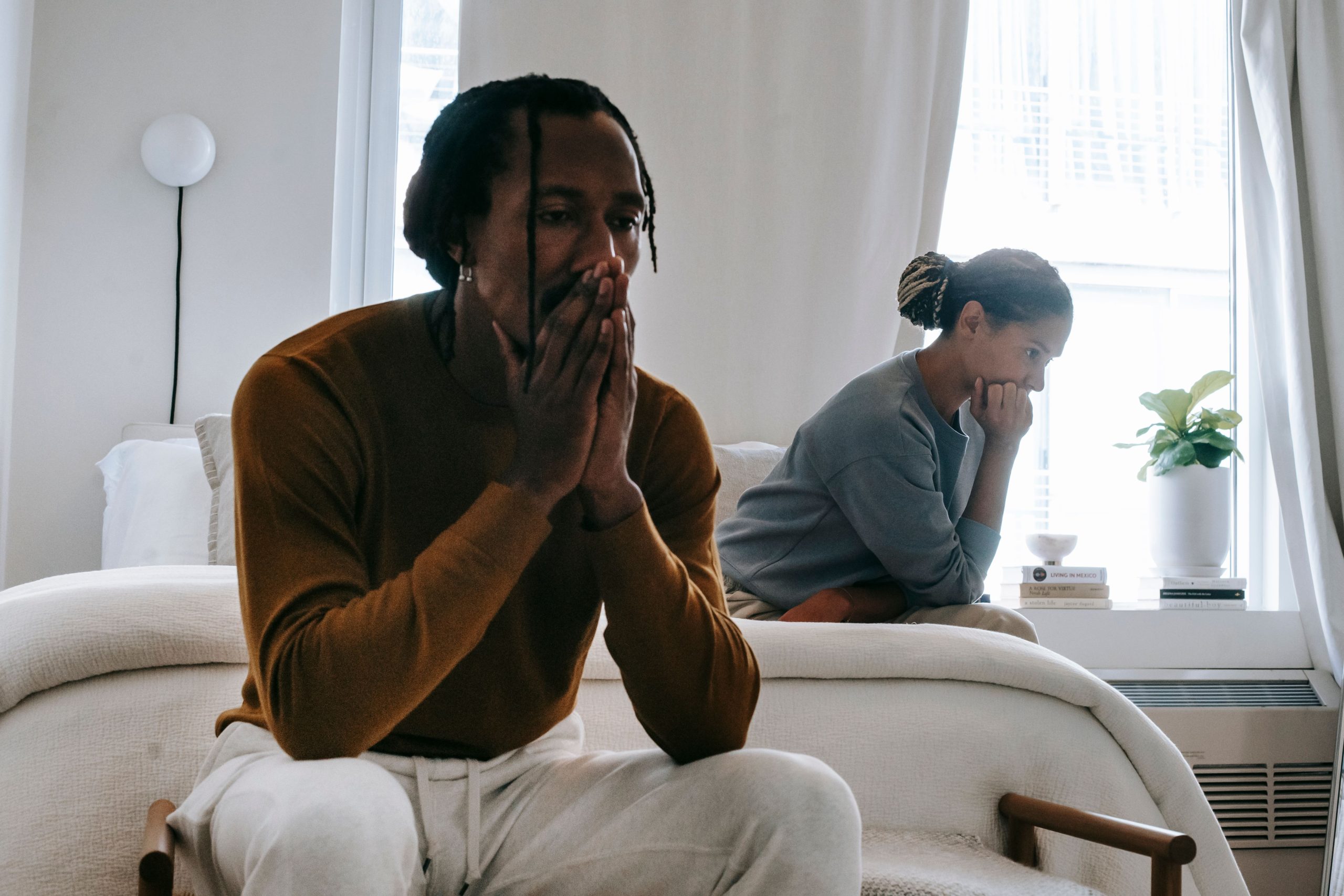 Wistful concerned African American couple in casual clothing sitting on bed at home after having quarrel --- Un couple afro-américain pensif et préoccupé en tenue décontractée assis sur un lit à la maison après une querelle.