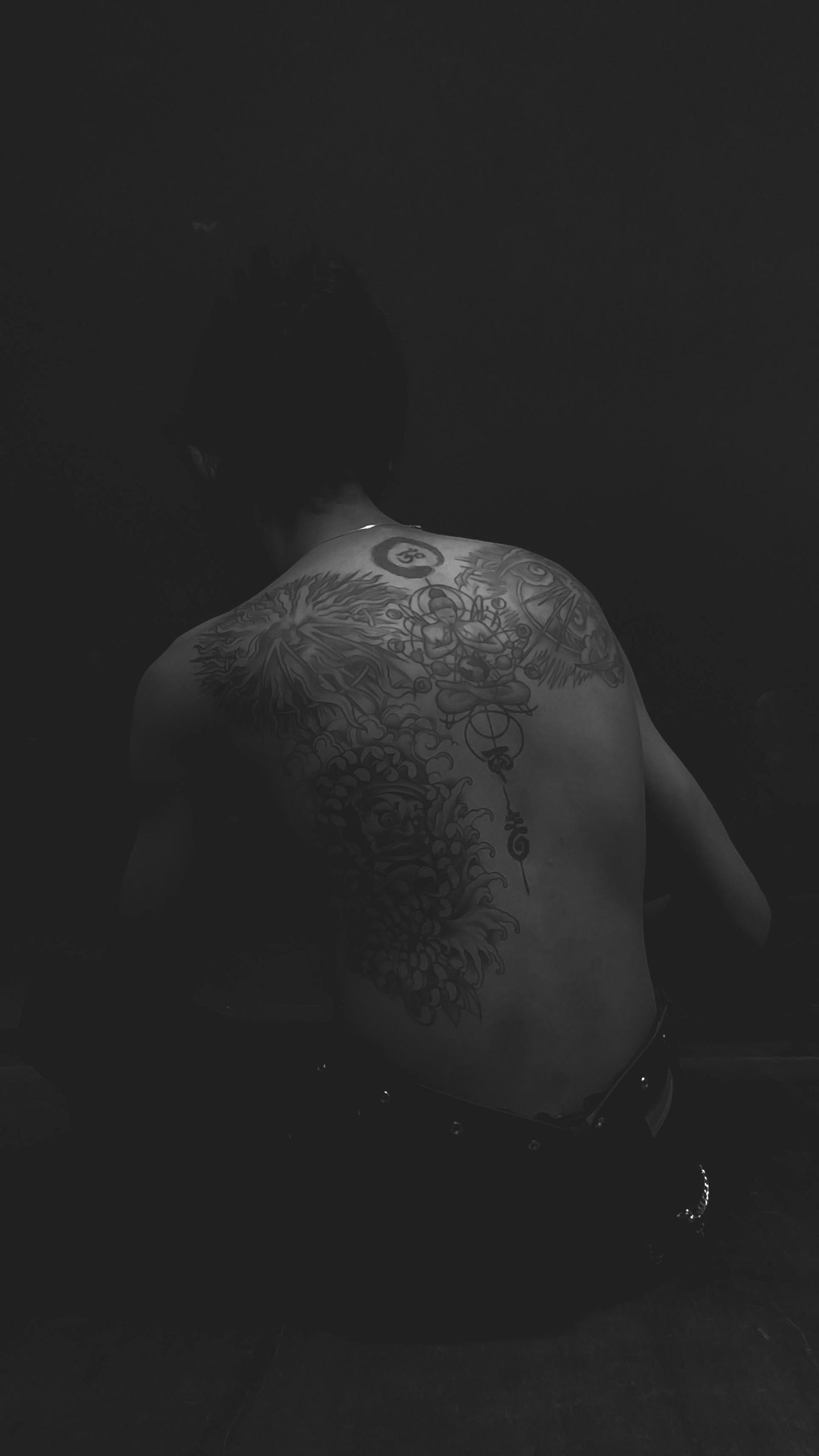 Artistic grayscale image featuring intricate tattoos on a man's back. Image en niveaux de gris artistique mettant en vedette des tatouages complexes sur le dos d'un homme.