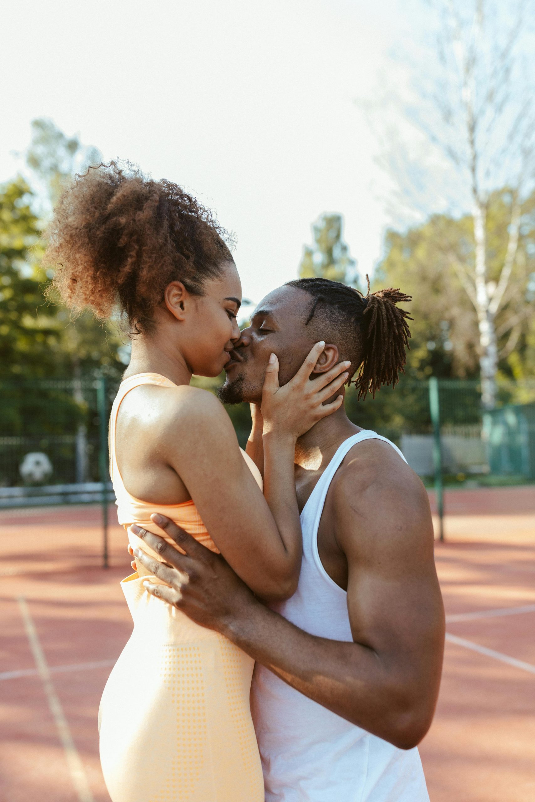 Loving couple sharing a kiss on a sunny tennis court. Outdoor romance. Un couple aimant partageant un baiser sur un court de tennis ensoleillé. Romance en plein air.