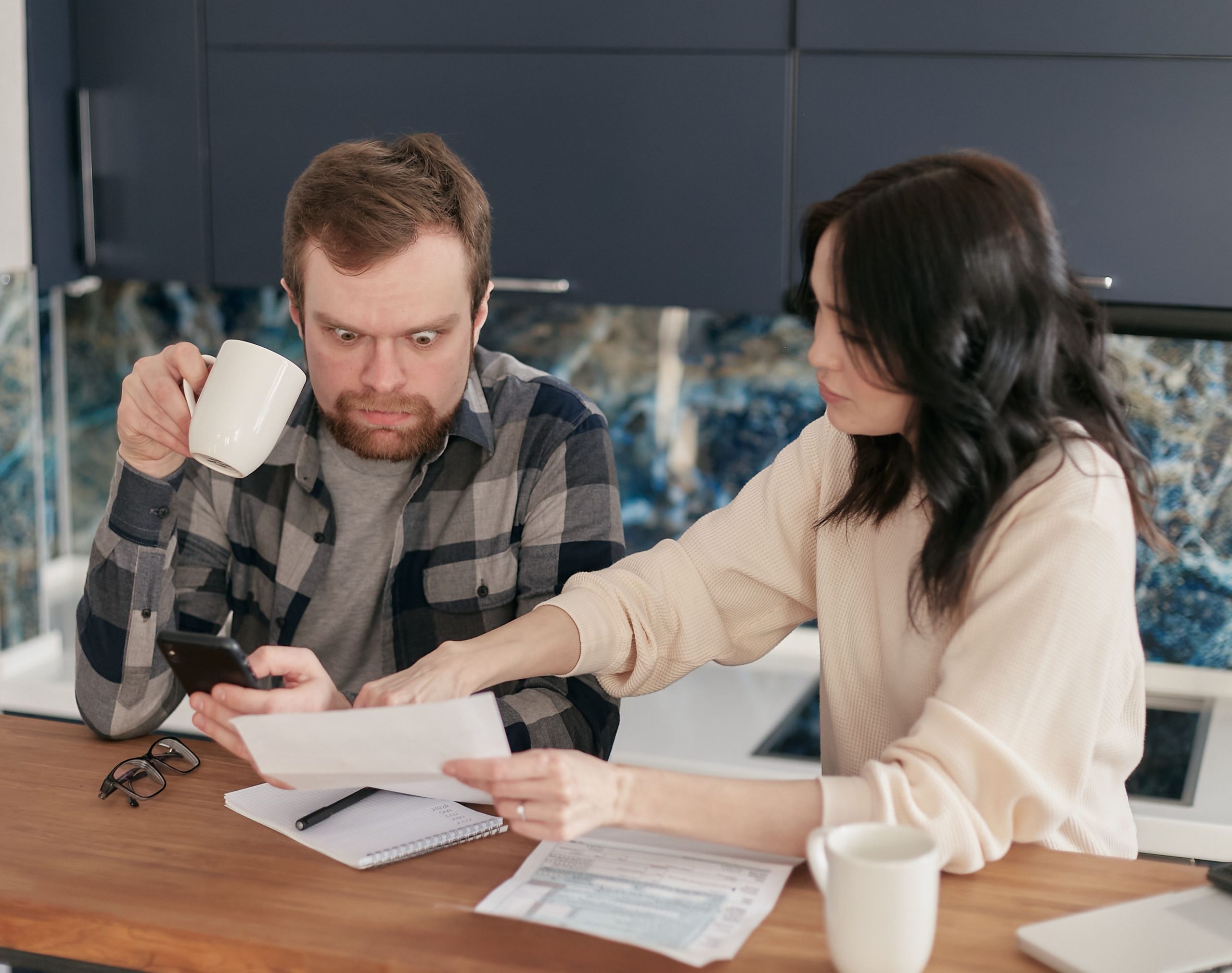 A couple reviews household bills in a kitchen, appearing concerned and focused. Un couple examine des factures domestiques dans une cuisine, semblant préoccupé et concentré.