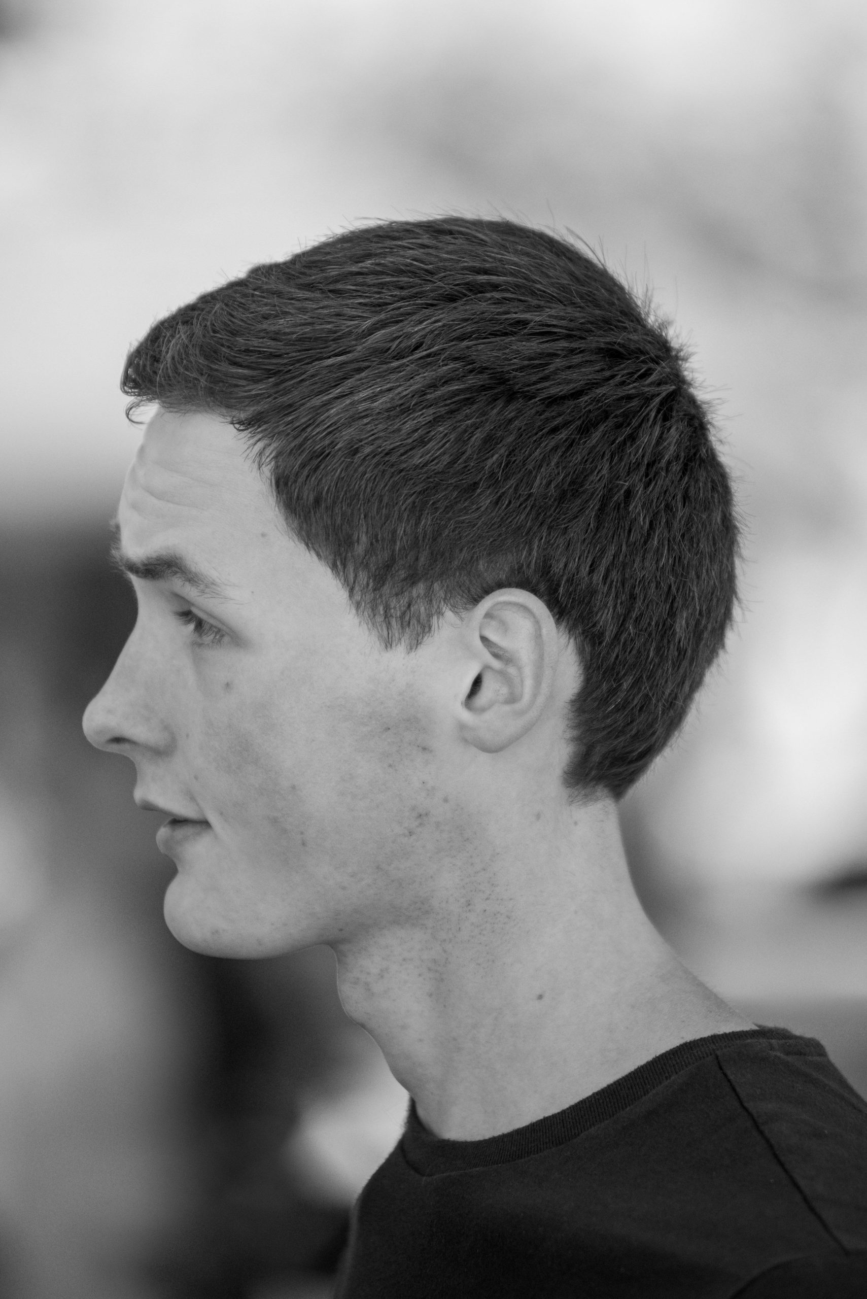 A grayscale side profile of a young man showcasing his hairstyle and thoughtful expression. Un profil latéral en niveaux de gris d'un jeune homme mettant en valeur sa coiffure et son expression pensif.