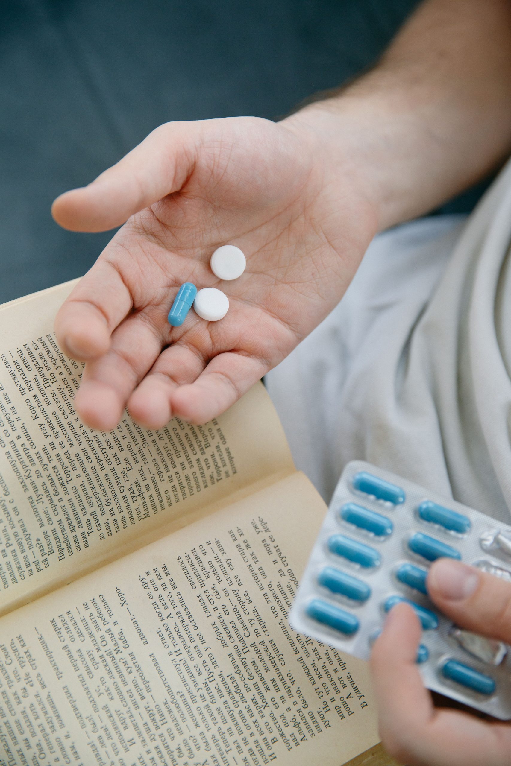 Person holding pills and a book in an intimate, close-up setting indoors. Personne tenant des pilules et un livre dans un cadre intime et rapproché en intérieur.