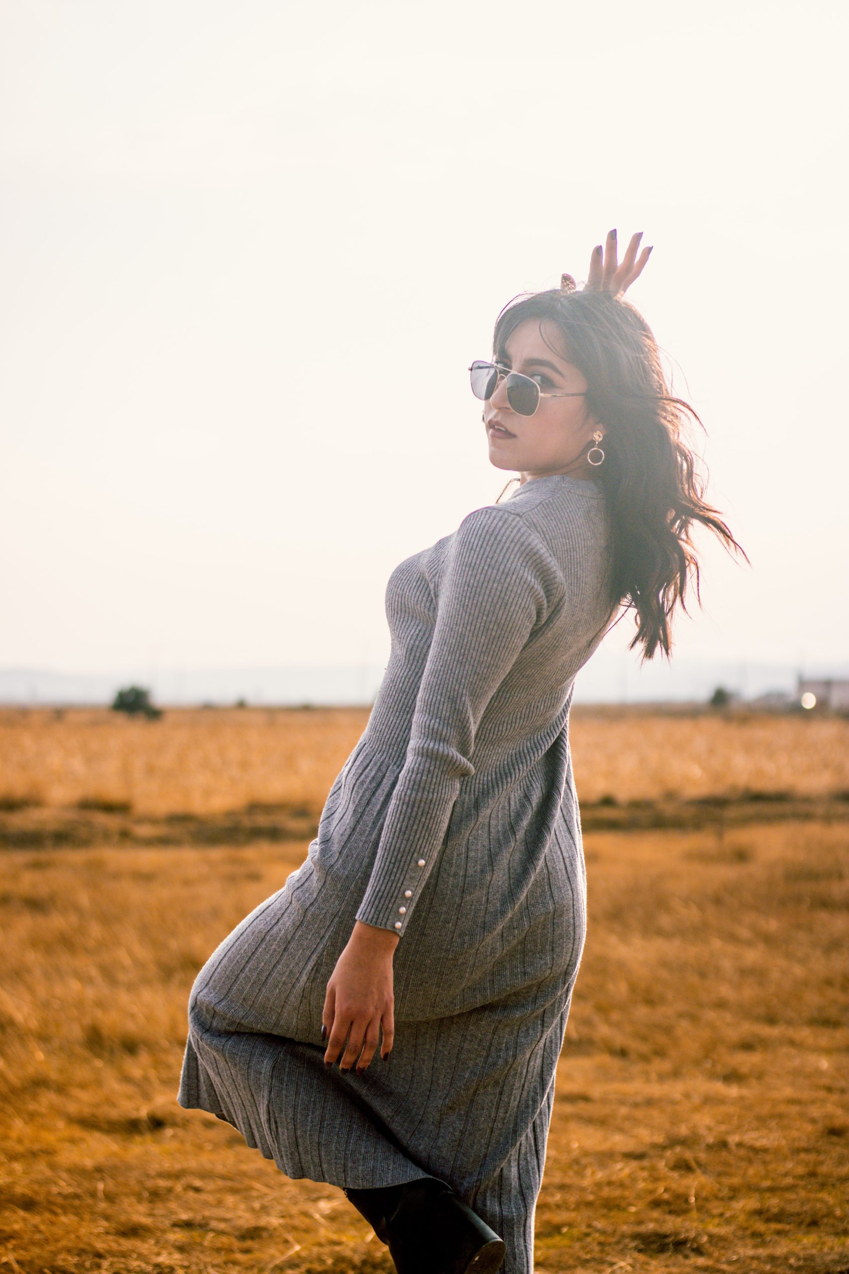 Stylish woman in sunglasses and long dress poses gracefully in a sunlit field. Femme élégante en lunettes de soleil et robe longue posant gracieusement dans un champ ensoleillé.