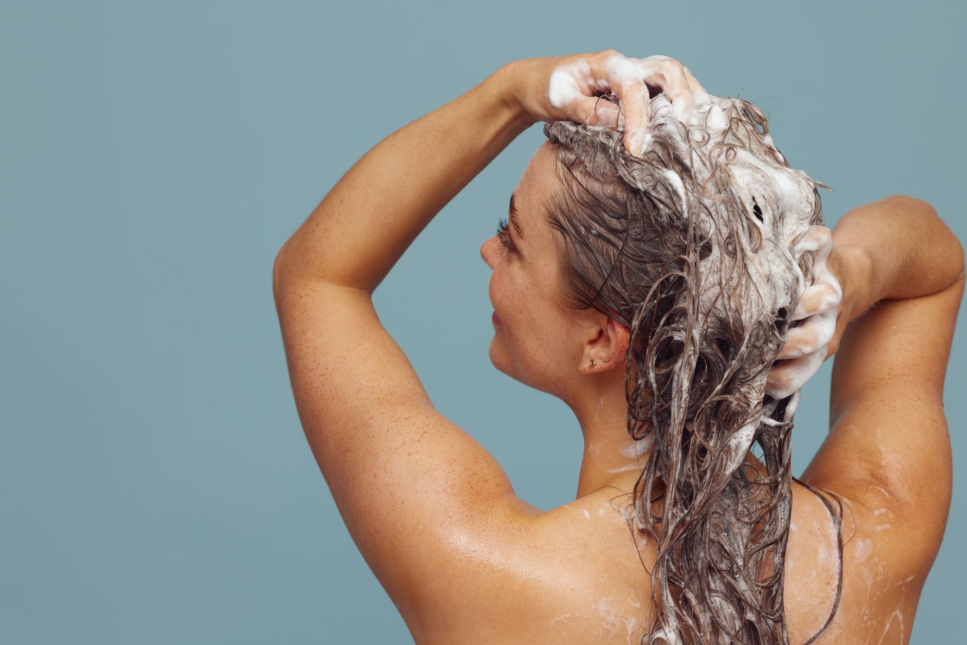 Femme qui masse un shampoing sur ses racines sous la douche