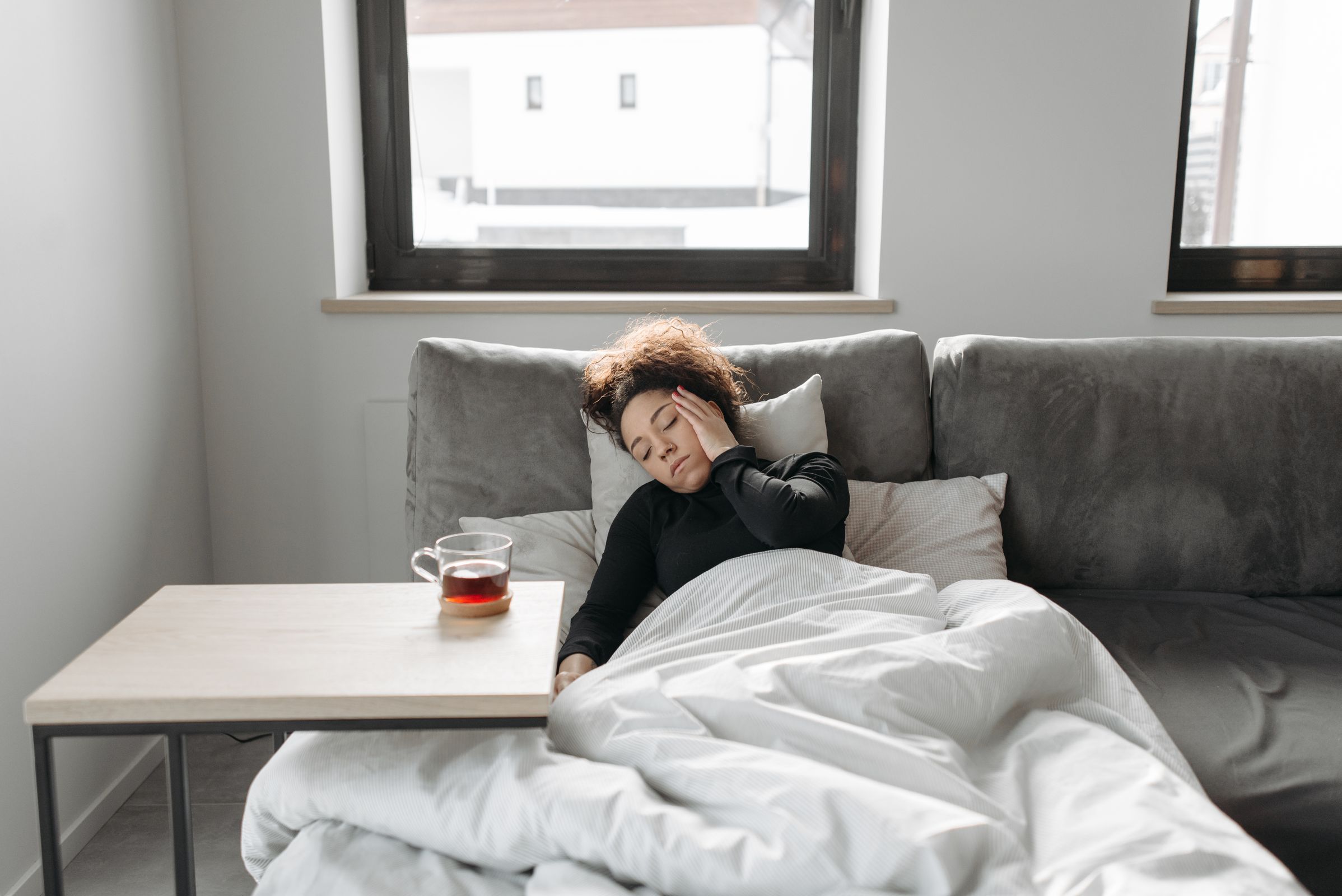 Femme malade allongée sur un canapé avec une tasse de thé