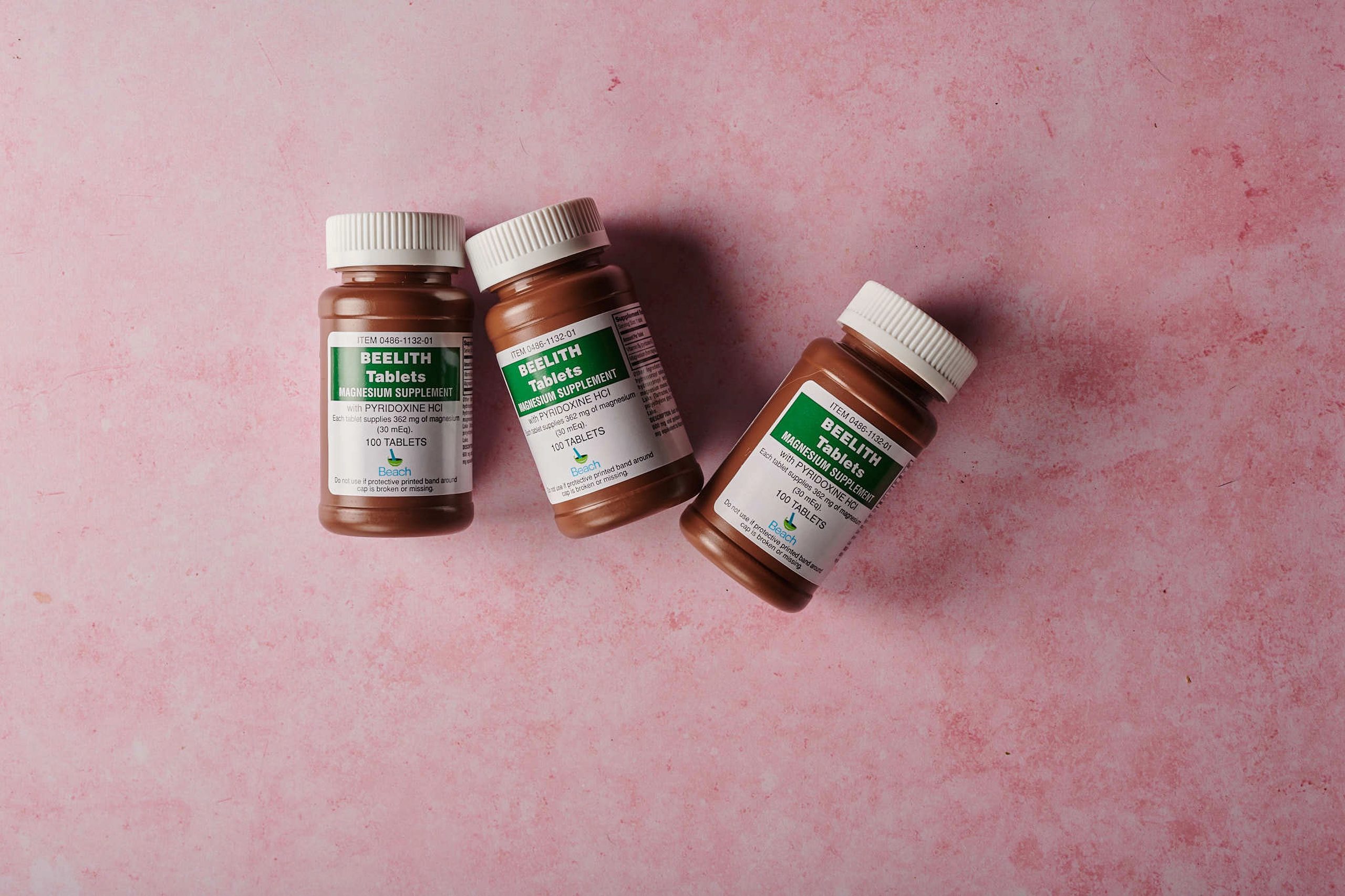 Three brown bottles of magnesium tablets on a soft pink background, ideal for health-themed content. Trois flacons bruns de comprimés de magnésium sur un fond rose doux, idéal pour le contenu lié à la santé.