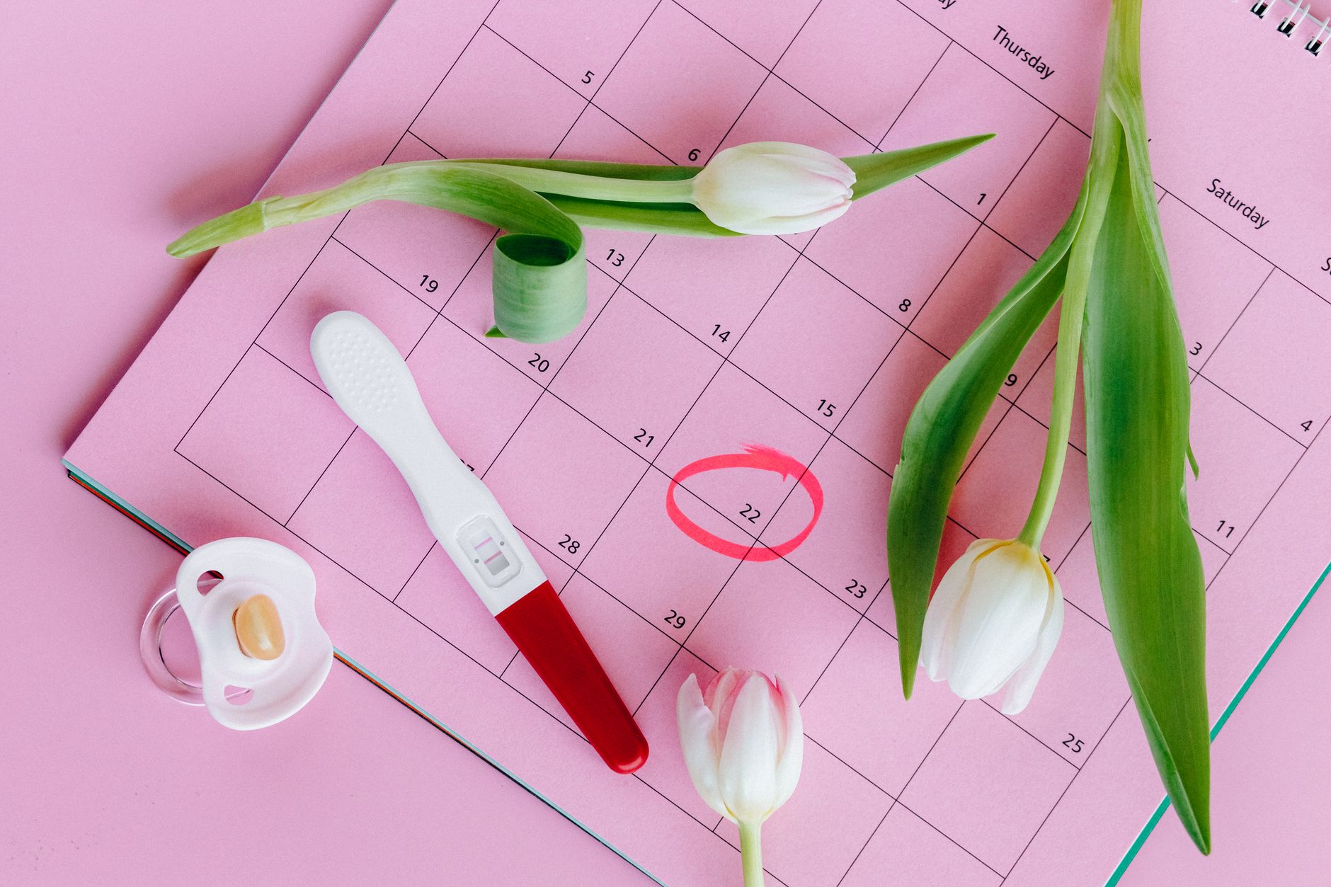 Test de grossesse posé sur un calendrier fleuri