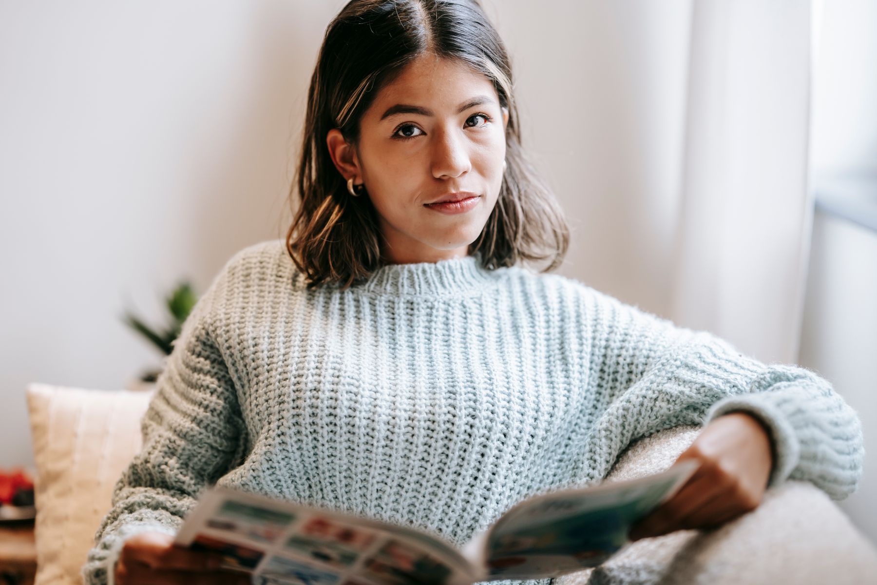 Femme installée dans un canapé en train de lire un magazine