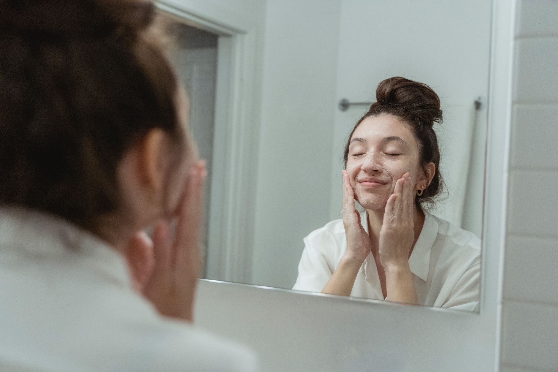 Femme appliquant un savon doux sur son visage devant le miroir